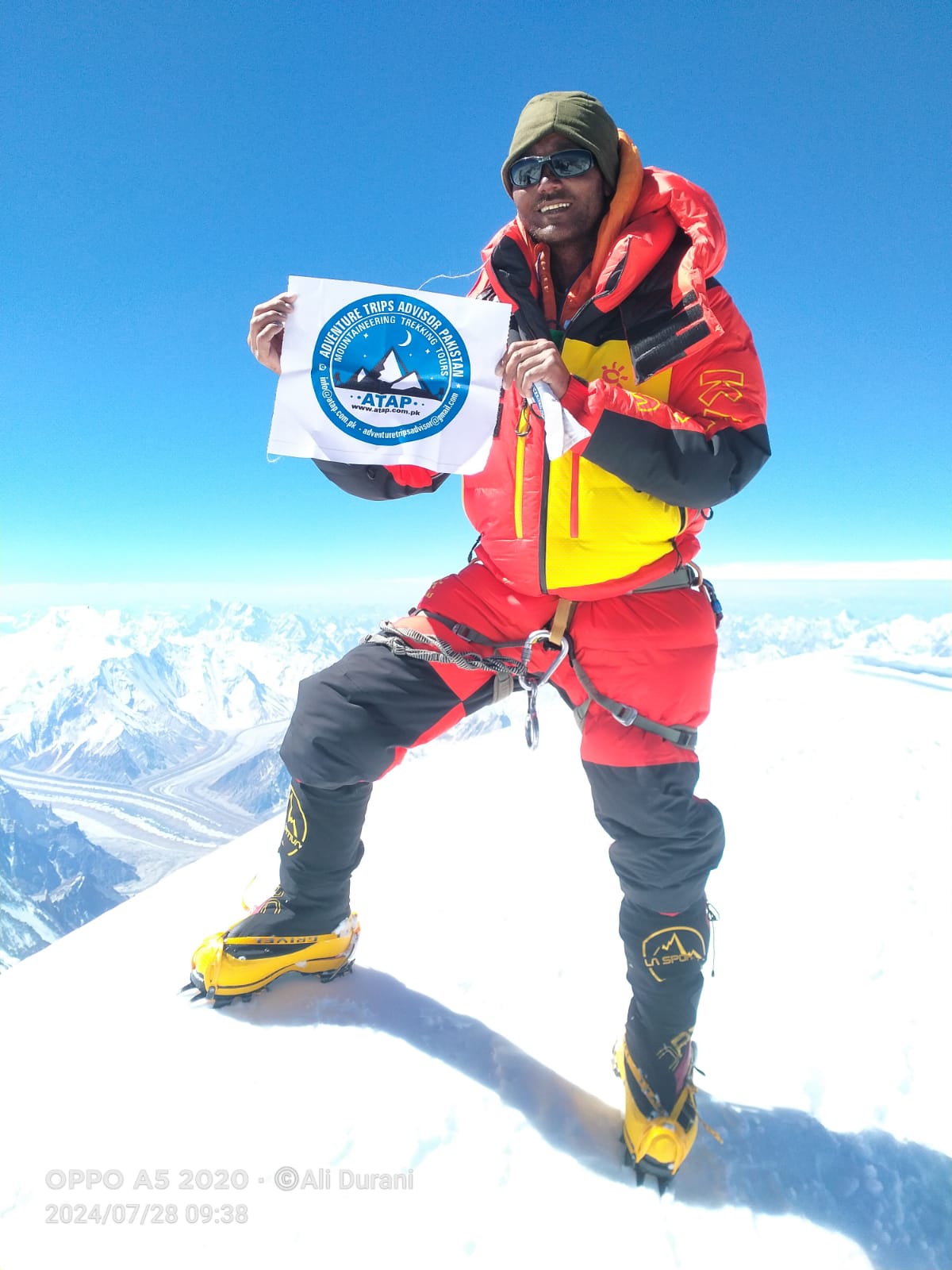 A victorious mountaineer holding a flag of ATAP K2, the second-highest mountain on Earth, after an extreme expedition through harsh terrain.